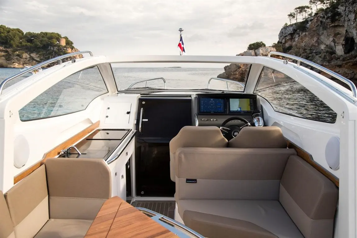 Interior of a modern boat, featuring a sleek dashboard with navigation screens, comfortable seating, and a view of the coastline.